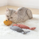 Cat playing with colorful fish-shaped toys on a white rug, featuring a gray tabby cat and plush fish toys. Perfect pet accessories for playful cats.