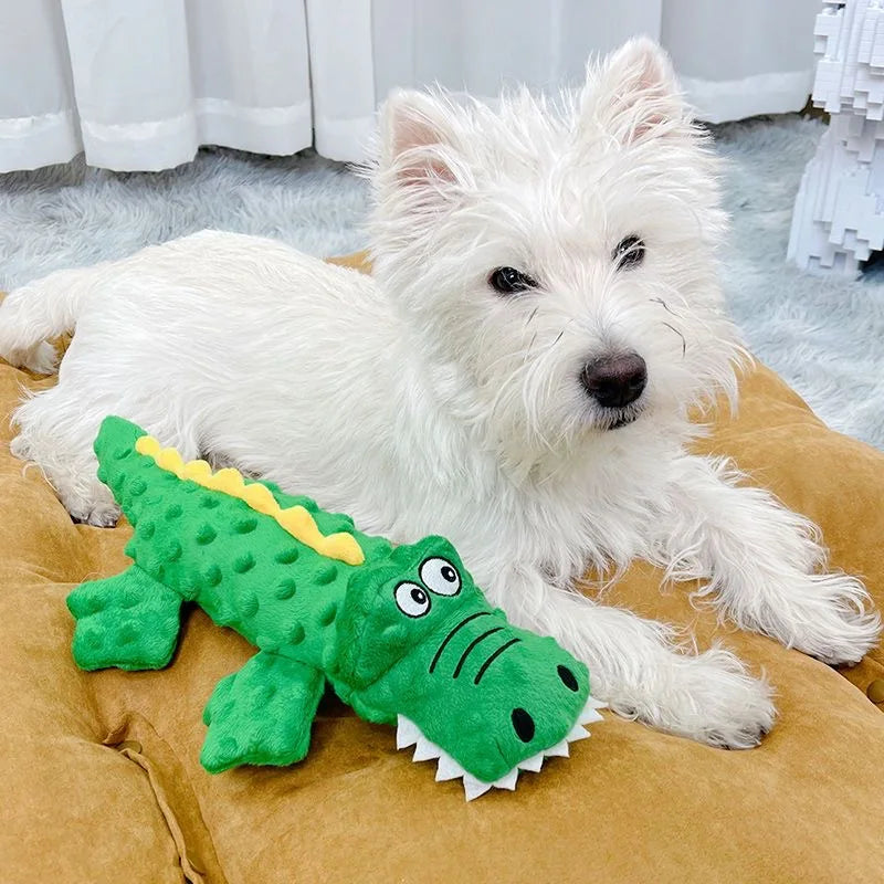 White terrier dog with green crocodile plush toy on brown cushion, fluffy carpet background. Cute pet, dog toy, home decor.