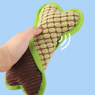 Hand squeezing a plush dog toy shaped like a bone, featuring a textured surface and green trim, against a blue background. Perfect for pet playtime.