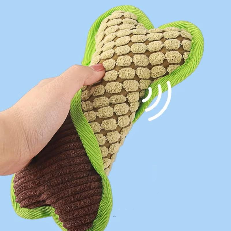 Hand squeezing a plush dog toy shaped like a bone, featuring a textured surface and green trim, against a blue background. Perfect for pet playtime.