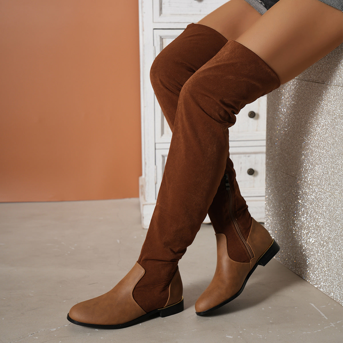 Brown over-the-knee suede boots with low heels, featuring a side zipper, styled against a neutral background. Fashionable women's footwear.