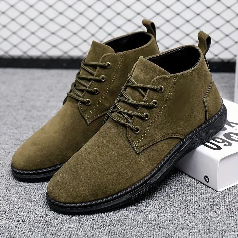 Olive green suede men's chukka boots with black soles, lace-up design, displayed on a gray carpet with a geometric background. Stylish casual footwear.