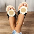 Women's sandals with daisy flower design, black straps, and beige soles on wooden floor. Perfect for summer fashion and casual wear.