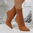 Brown suede ankle boots with clear block heels on a white surface, featuring a pointed toe design. Fashionable women's footwear, stylish boots.