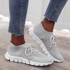 Gray knit slip-on sneakers with white soles, worn with frayed hem jeans. Stylish, breathable footwear for casual wear. Perfect for walking or running.