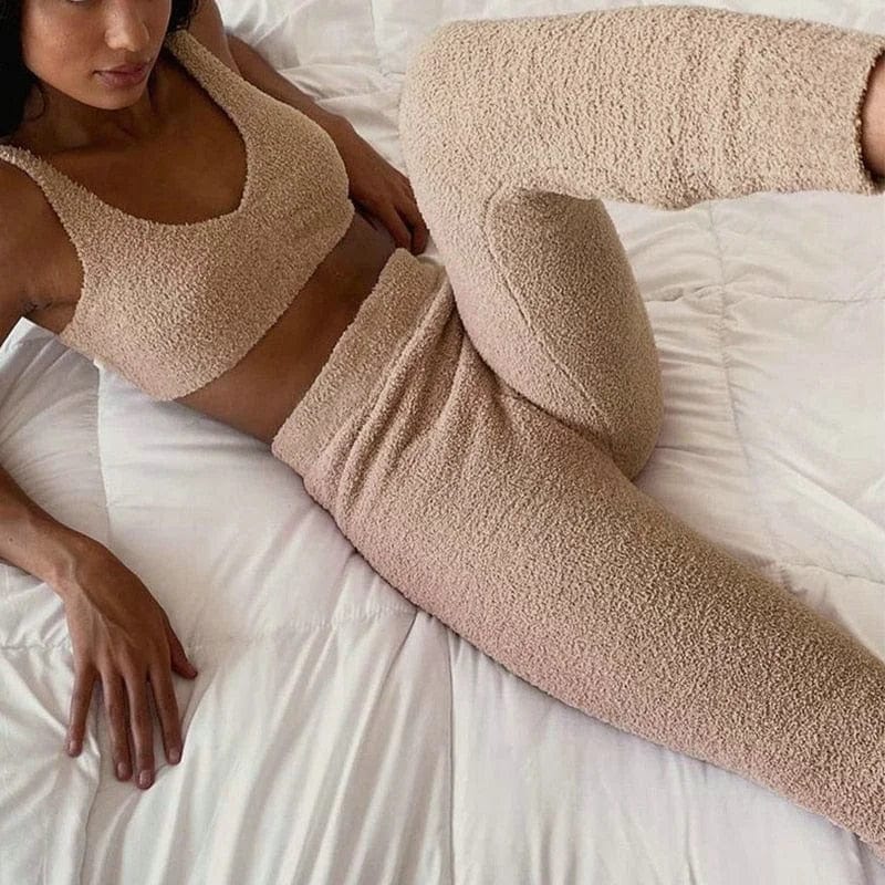 Woman in cozy beige fleece sports set lounging on a white bed. Fluffy activewear, comfortable loungewear, stylish workout outfit.