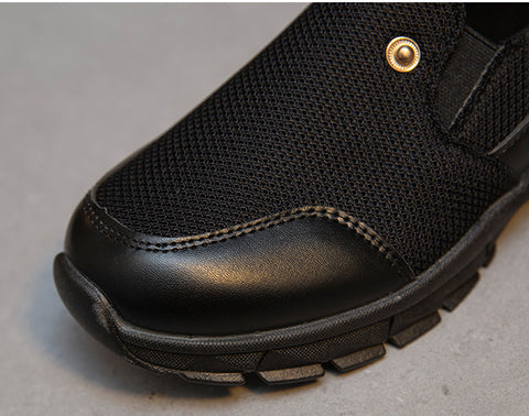 Black mesh slip-on shoe with rugged sole, leather accents, and gold rivet detail. Ideal for outdoor activities and casual wear. Durable and stylish footwear.