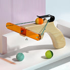 Cat toy ball launcher with wooden handle and orange acrylic arm, featuring colorful plush balls. Ideal for interactive pet play and exercise.