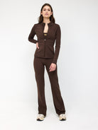 Woman wearing brown zip-up jacket and matching pants, standing confidently. Fashionable activewear outfit, perfect for casual or workout settings.