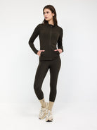 Woman wearing dark olive zip-up jacket and leggings set, standing with hands in pockets. Stylish activewear outfit, perfect for fitness and casual wear.