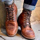 Brown leather men's lace-up boots, vintage style, worn with rolled-up jeans.