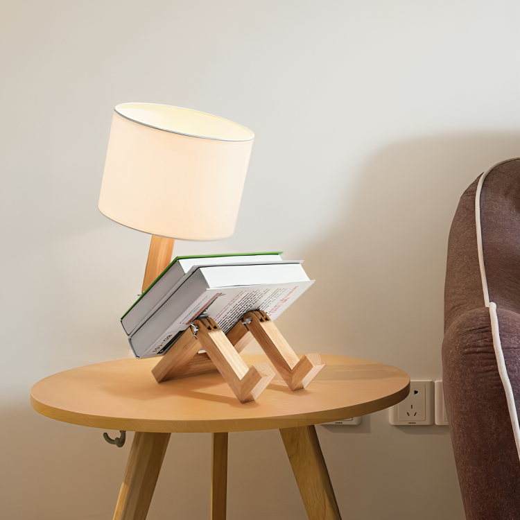 Modern wooden table lamp with a unique book-shaped design on a round wooden side table, next to a brown sofa. Ideal for stylish home decor.