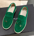 Green suede loafers with gold accents on a black Saint Laurent Paris box, featuring a sleek design and white soles, perfect for stylish casual wear.