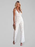 White lace jumpsuit with spaghetti straps and flared legs, accessorized with a beige clutch and jewelry. Perfect for summer fashion and elegant events.