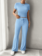 Woman wearing a light blue two-piece lounge set with short-sleeve crop top and drawstring pants, paired with white sneakers, standing indoors.