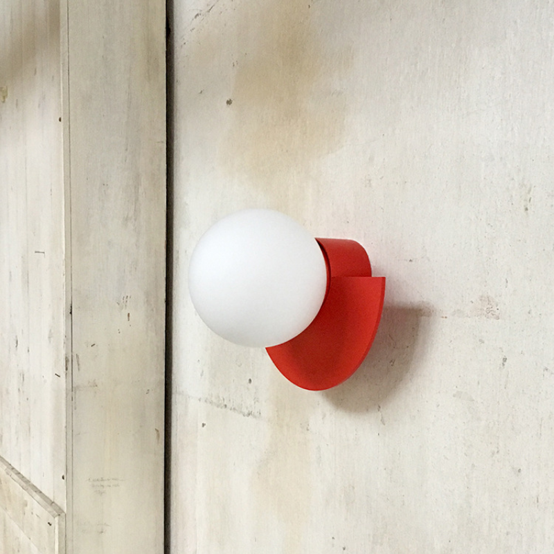 Modern red wall sconce with a round white globe light fixture, mounted on a textured beige wall. Contemporary lighting design, minimalist decor.