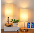 Modern bedside table lamps with USB charging ports, wooden base, and fabric shade, illuminating a cozy bedroom setting with a small potted plant.