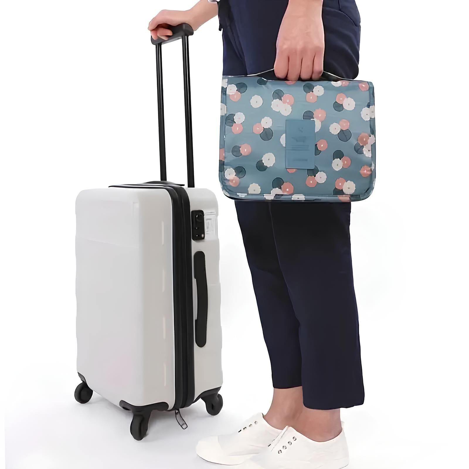 Person holding a floral travel organizer and standing next to a white hard-shell suitcase with wheels, ideal for travel and luggage storage solutions.