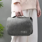 Woman holding a stylish gray travel toiletry bag with handle, featuring organized compartments for cosmetics and toiletries. Ideal for travel essentials.