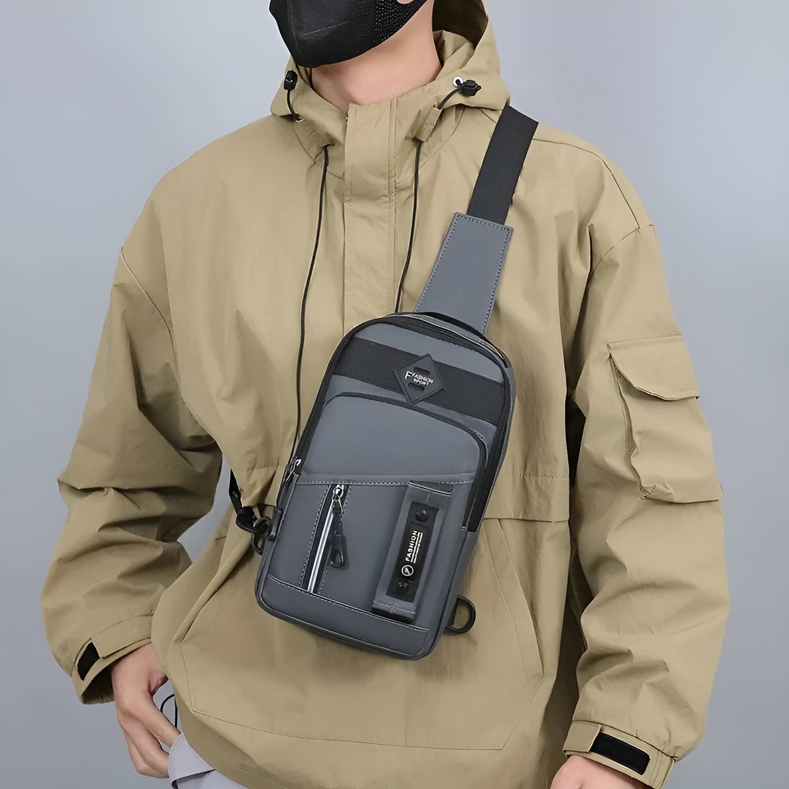 Man wearing a beige jacket and black face mask, showcasing a stylish gray crossbody sling bag with multiple compartments, ideal for urban fashion.