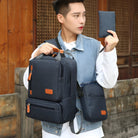 Young man holding a stylish black backpack and matching pouch, wearing a denim vest. Trendy urban fashion, casual travel accessories.