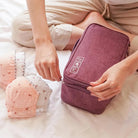 Woman organizing bras into a purple travel lingerie organizer bag on a bed. Efficient packing, travel essentials, lingerie storage solution.