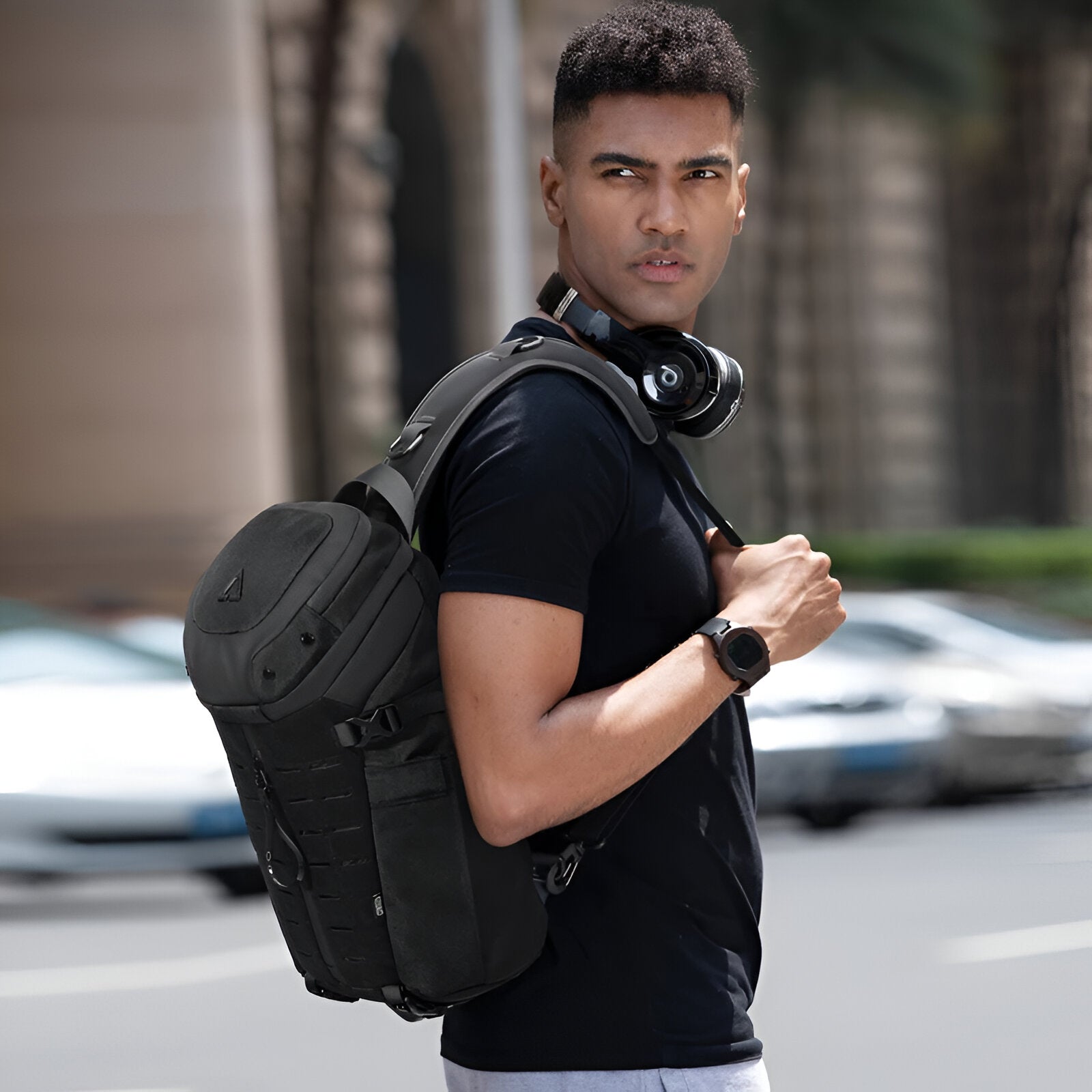 Man wearing black backpack and headphones, standing on city street. Stylish urban fashion, outdoor gear, modern accessories, casual attire.