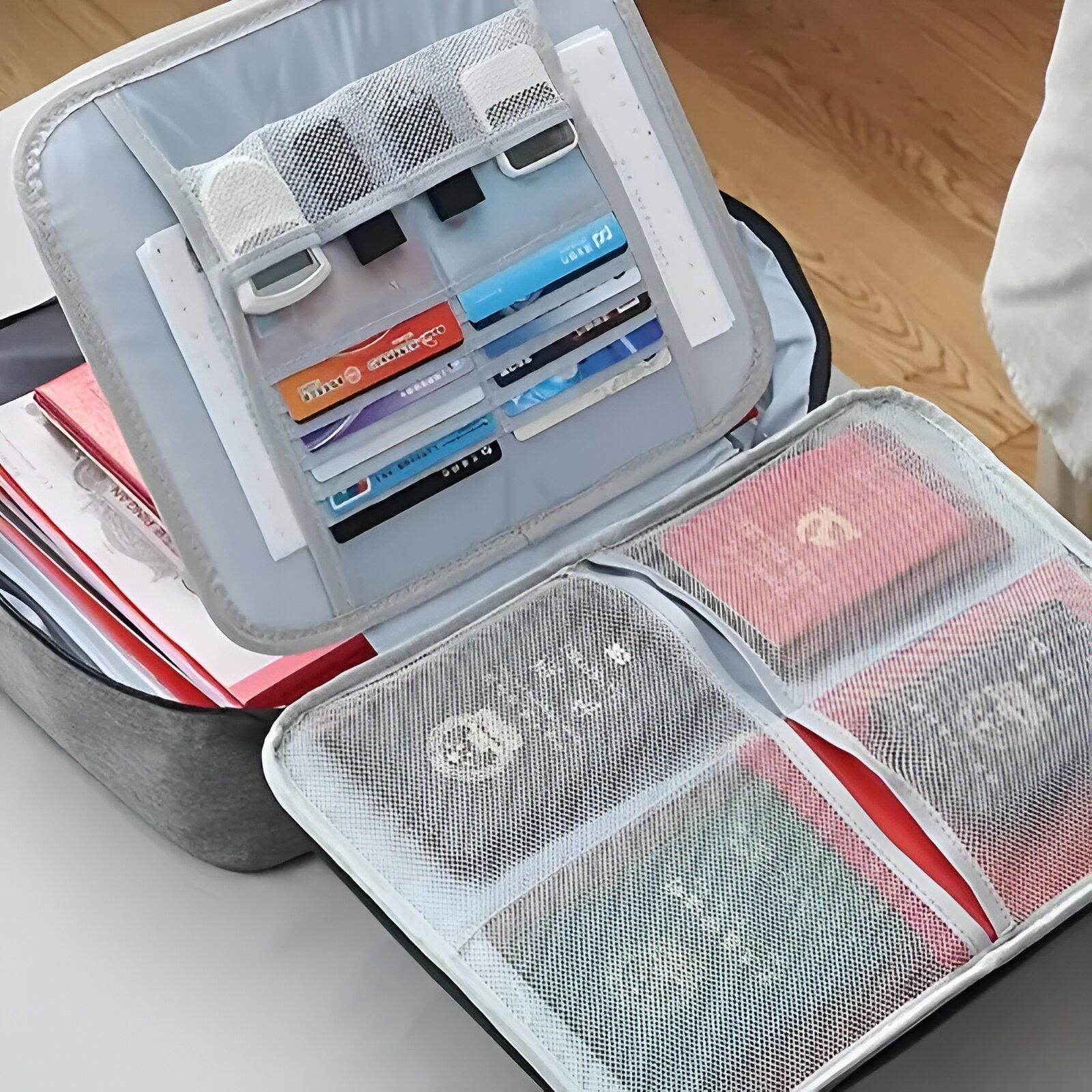 Open suitcase organizer with mesh pockets holding passports, travel documents, and credit cards on a wooden floor. Travel essentials storage solution.