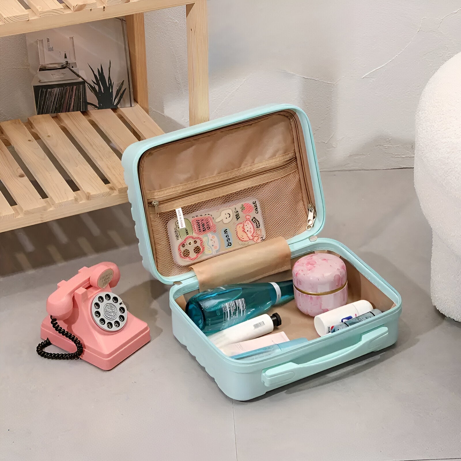 Open light blue travel makeup case with skincare products and toiletries, next to a vintage pink rotary phone on a wooden shelf.