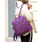 Woman carrying a stylish purple convertible backpack purse with multiple zippered compartments, perfect for travel and everyday use. Fashionable and functional.