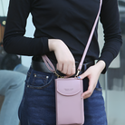 Woman holding a stylish pink crossbody phone bag, wearing casual black top and jeans. Fashionable accessory for women, perfect for on-the-go convenience.