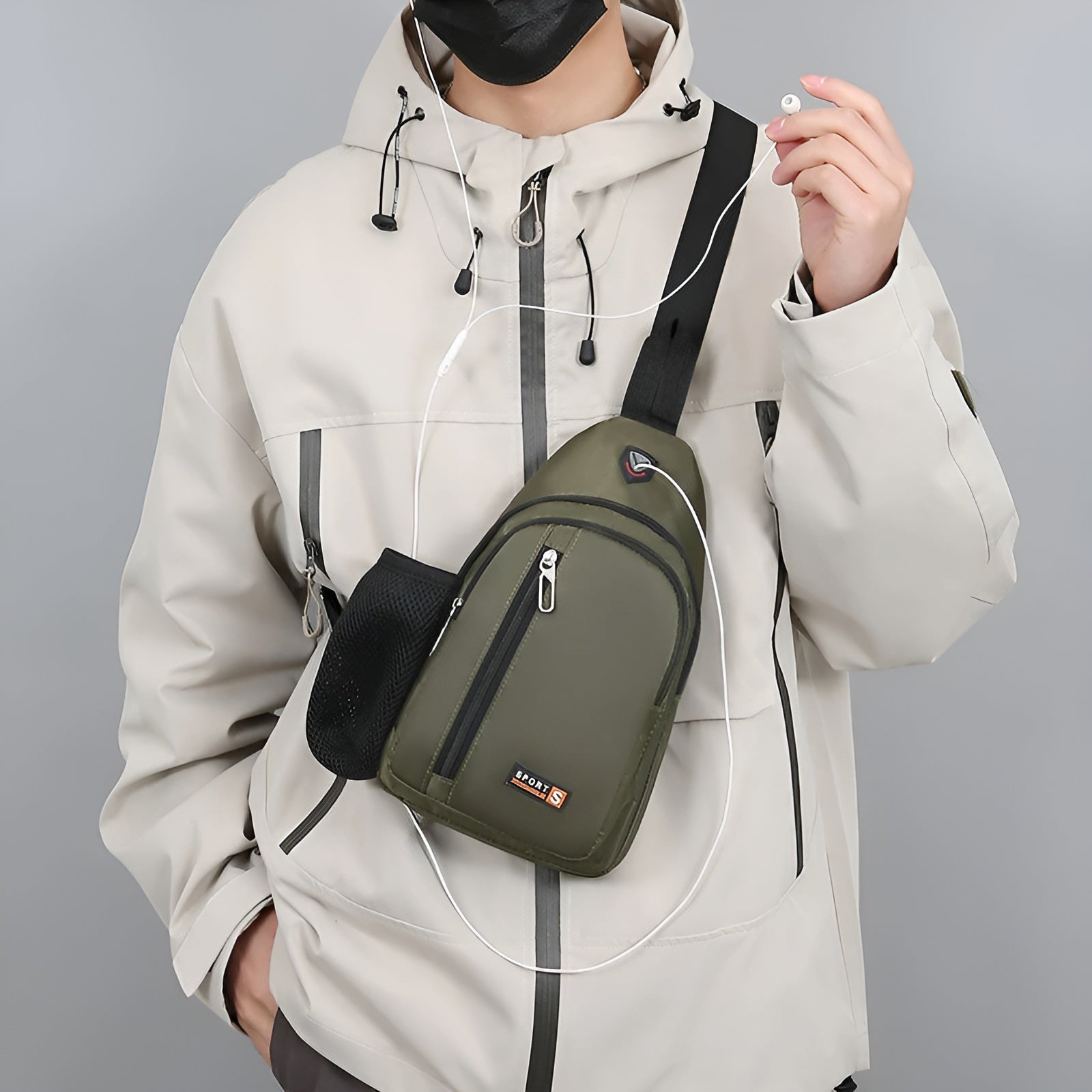 Person wearing a beige jacket with a green crossbody sling bag, holding earphones. Stylish urban fashion, practical accessory for travel and daily use.