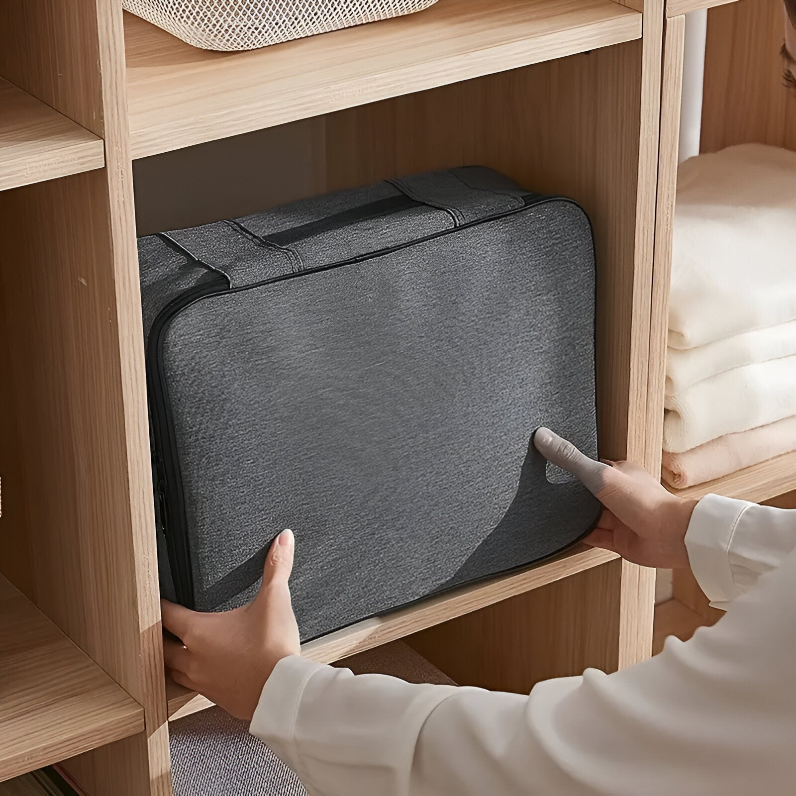 Gray fabric storage bag being placed on a wooden shelf, ideal for organizing clothes and accessories. Durable, space-saving home storage solution.