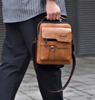 Man carrying stylish brown leather crossbody bag with front pocket and adjustable strap, ideal for travel and daily use. Fashionable men's accessory.