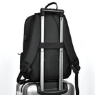 Black travel backpack securely attached to a silver rolling suitcase handle, showcasing convenient luggage strap feature for easy airport travel.