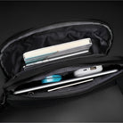 Open black travel organizer bag with multiple compartments, holding a notebook, pen, power bank, and electronic accessories. Ideal for tech-savvy travelers.