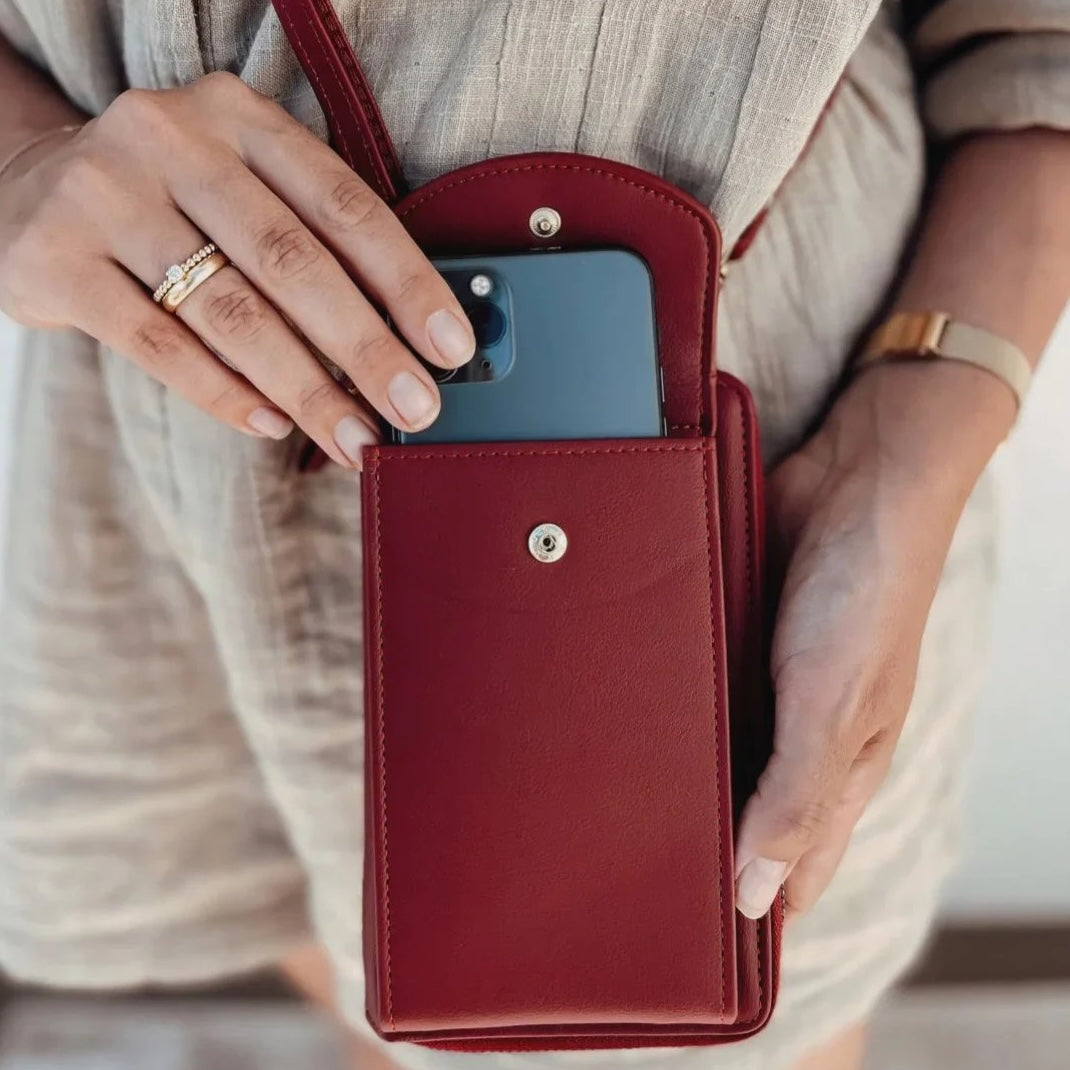 Woman holding a red leather crossbody phone bag with a smartphone inside, showcasing stylish and functional accessory for modern convenience.