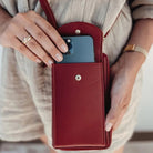 Woman holding a red leather crossbody phone bag with a smartphone inside, showcasing stylish and functional accessory for modern convenience.