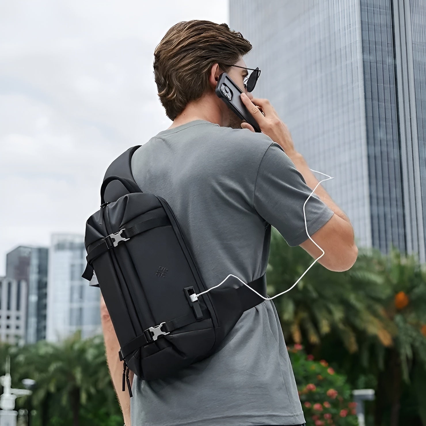 Man using a black anti-theft crossbody sling bag with USB charging port, standing in an urban setting. Stylish travel backpack for tech-savvy commuters.