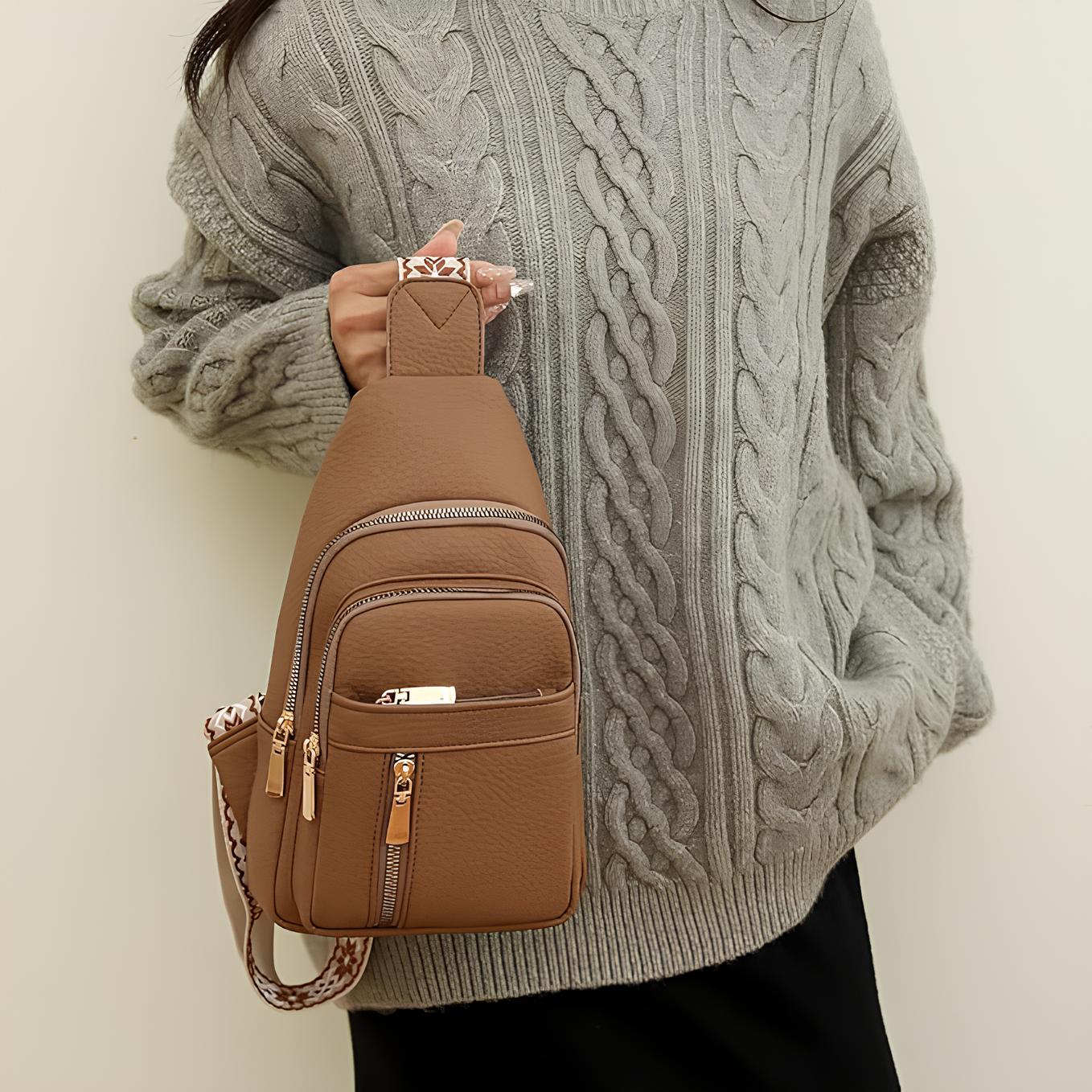 Woman in gray cable knit sweater holding a brown leather crossbody bag with multiple zippered compartments and patterned strap. Fashion accessory.