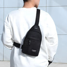 Man wearing a black crossbody sling bag with "Fashion" label, adjustable strap, and zipper pocket, paired with a white sweatshirt. Stylish urban accessory.