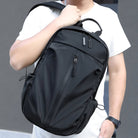 Man holding sleek black backpack with multiple compartments, wearing a white t-shirt. Perfect for travel, school, or work. Durable and stylish design.