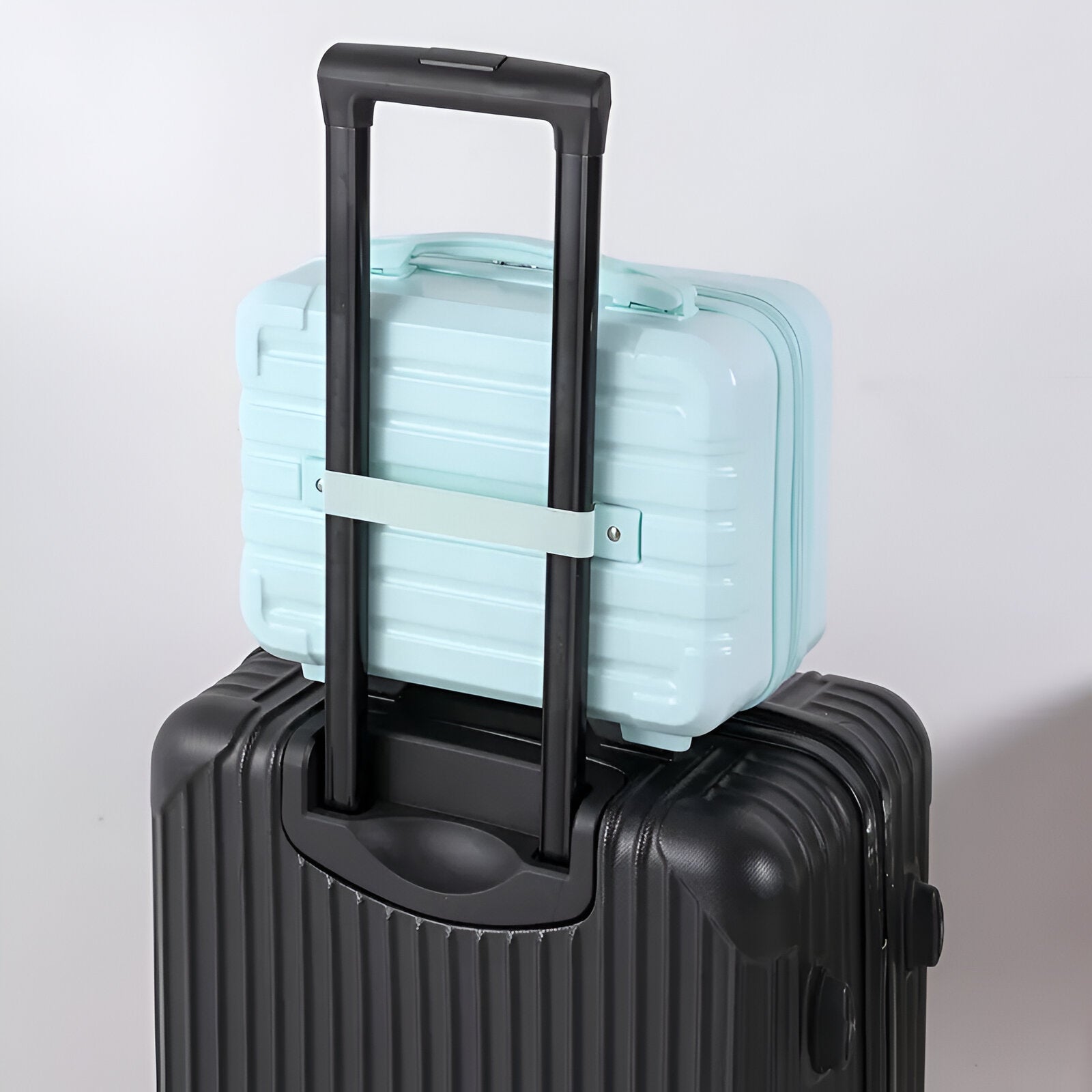 Light blue hard-shell carry-on suitcase secured on top of a black rolling luggage with telescopic handle, ideal for travel and business trips.