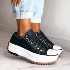 Black platform sneakers with white soles and jagged edges, worn with rolled-up jeans. Trendy footwear for casual fashion and street style.