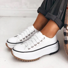 White platform sneakers with thick soles and black trim, worn with rolled-up pants. Trendy women's footwear, casual style, comfortable design.