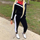 Woman wearing a black and white classic tracksuit set with red accents, standing outdoors on a sidewalk. Fashionable athletic wear, casual style.