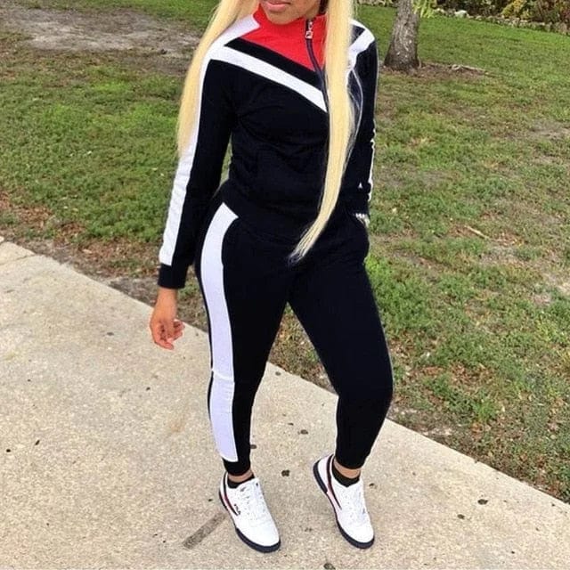 Woman wearing a black and white classic tracksuit set with red accents, standing outdoors on a sidewalk. Fashionable athletic wear, casual style.