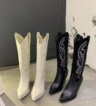 White and black knee-high leather cowboy boots for women with intricate embroidery, displayed indoors. Fashionable Western footwear.