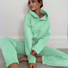 Woman wearing a loose green tracksuit with a cropped sweatshirt, sitting on the floor. Fashionable loungewear, cozy athleisure outfit.