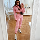 Woman in pink cropped sweatshirt and joggers set, taking a mirror selfie in a stylish room. Fashionable casual outfit, trendy athleisure wear.